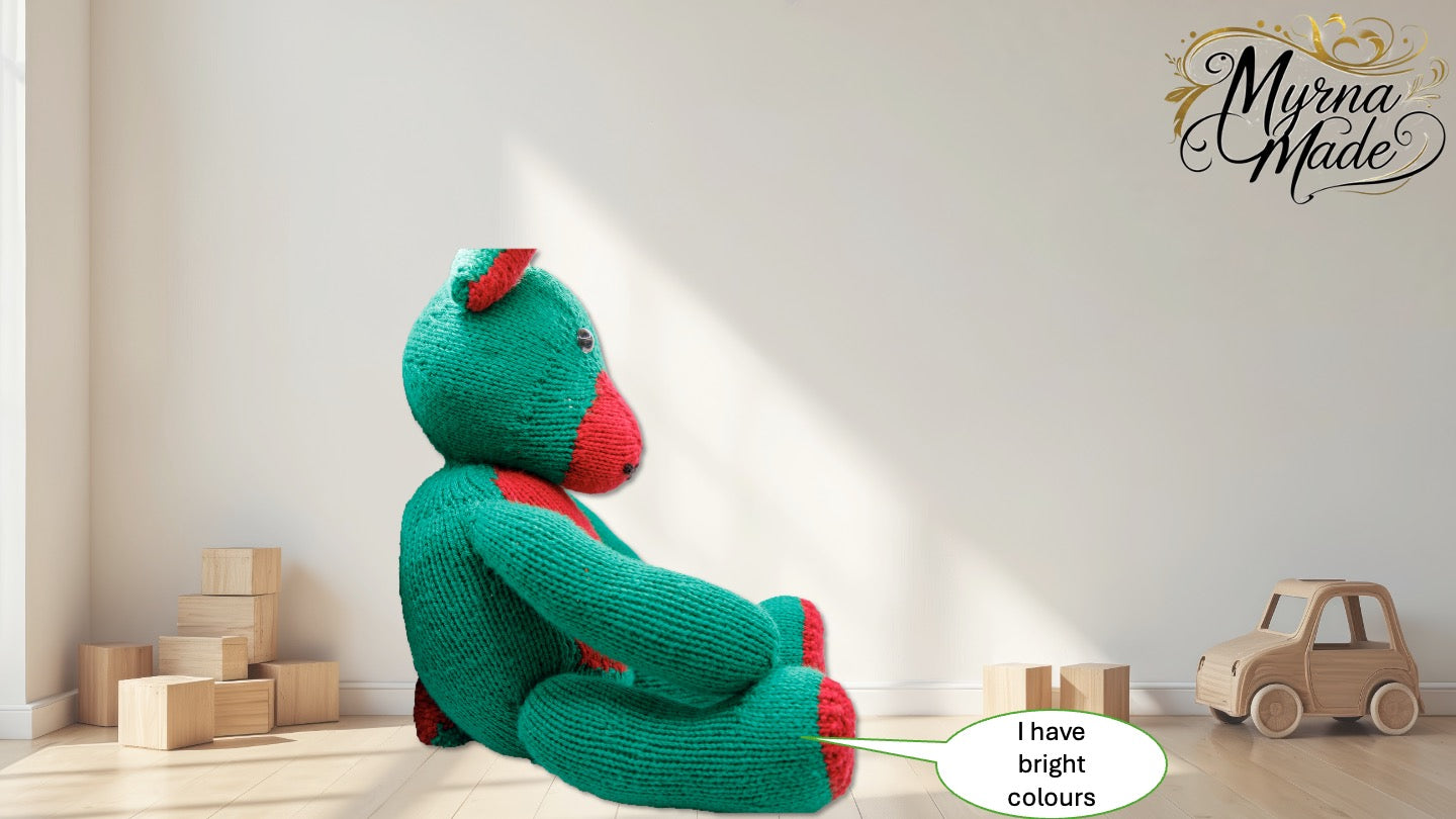 Green teddy bear with red accents sitting on a wooden floor with toys around, featuring 'Myrna Made' branding.